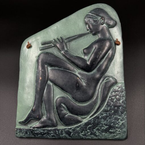 Pakabinamas keramikinis paveikslas vaizduojantis sėdinčią ir fleita grojančią moterį