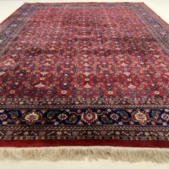 Persiškas raudonas vilnos rankų darbo kilimas, mėlynu apvadu su augaliniais ornamentais.