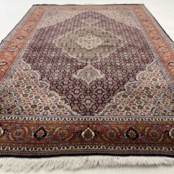 Rausvas persiškas vilnos rankų darbo kilimas su augaliniais ir geometriniais ornamentais.