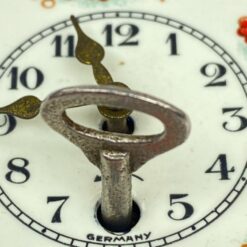 Mechaninis žalvario ir emaliuoto metalo miniatiūrinis sieninis laikrodis 4,5×6,5×12 cm